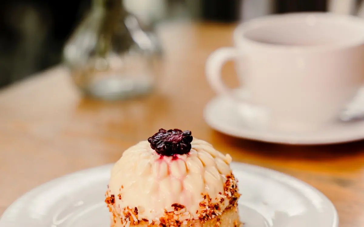 Postre flor de coco y zarzamora junto a una taza de café en una mesa de Macchiato